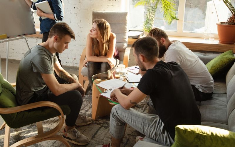 A group of a millennial workforce collaborating in a room of couches sharing a table