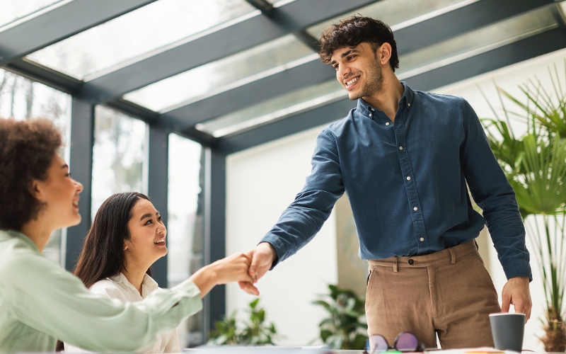 young man standing and shaking hands with woman seated in green shirt