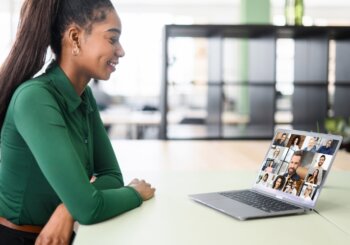 woman sitting at table talking with a group of people virtually on laptop