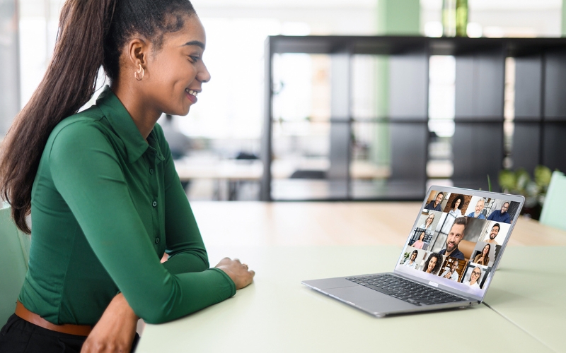 woman sitting at table talking with a group of people virtually on laptop