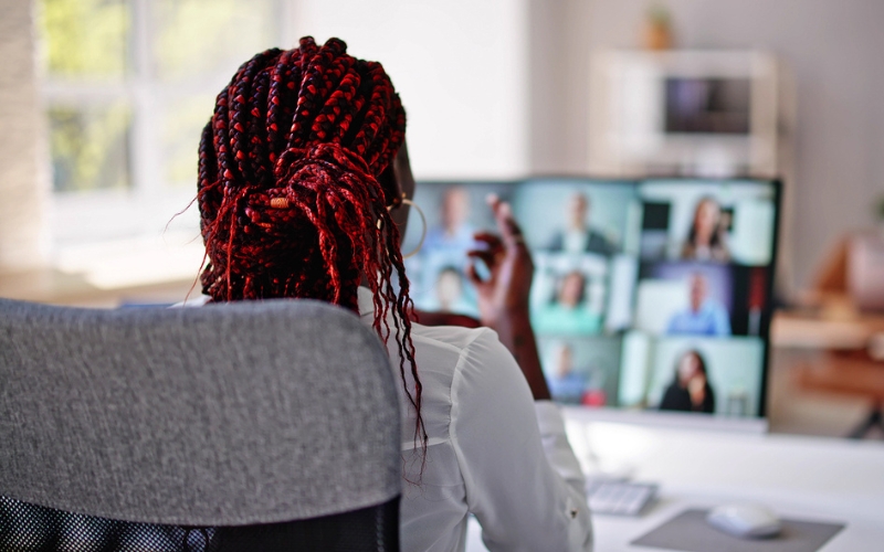 back of woman's head sitting at desk looking at a screen of multiple people in a virtual conference