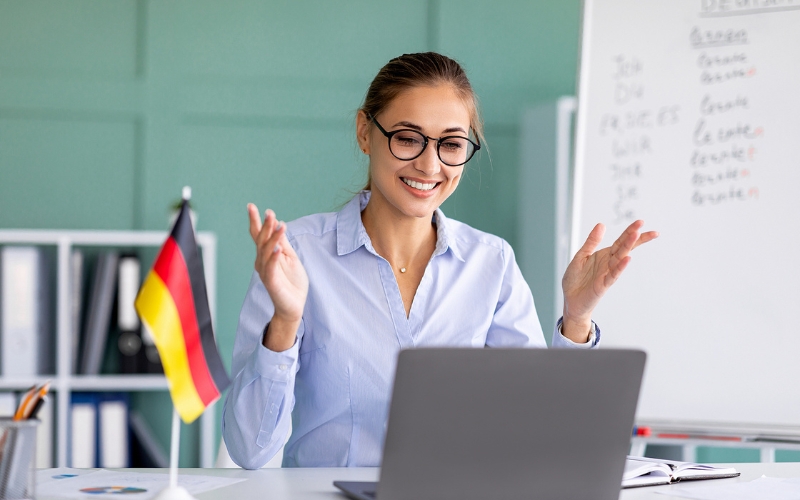woman in glasses talking on virtual call with german flag on desk and whiteboard behind her