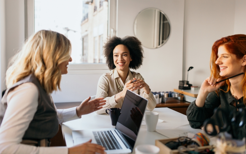 three colleagues conversing in an office with natural light and large window